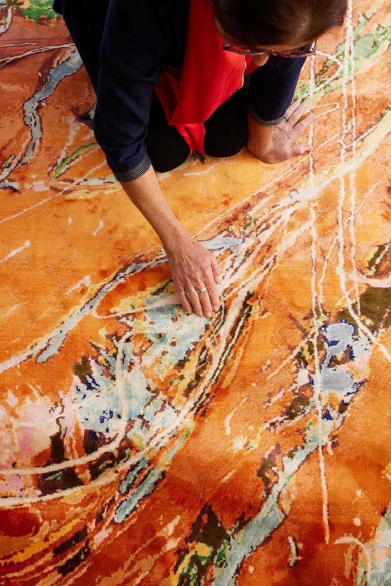 Australian artist Dena Lawrence inspects stunning orange and blue silk designer rug.